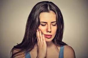 Dental Abscess Affiliated Orthodontics Peoria AZ Woman with long hair holding her jaw in pain, illustrating symptoms of a dental abscess.