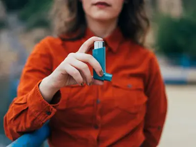 Young woman holding an asthma inhaler outdoors, highlighting the connection between asthma and oral health issues like cavities.