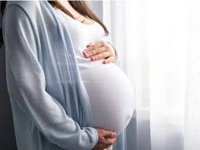 Pregnant woman gently cradling her baby bump, symbolizing the importance of oral health and wellness during pregnancy.